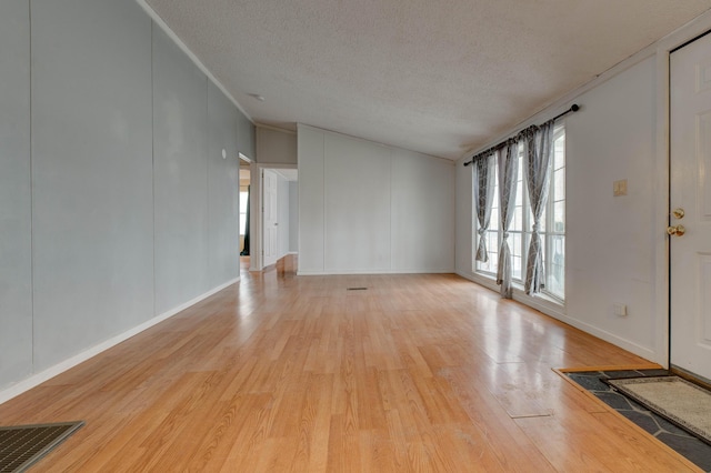 unfurnished living room featuring visible vents, light wood-style flooring, crown molding, a textured ceiling, and a decorative wall