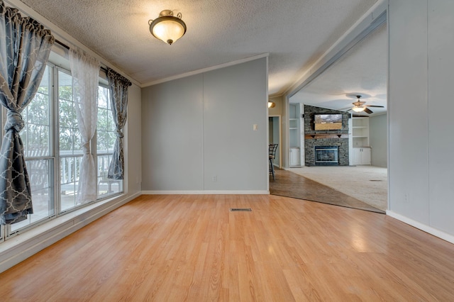 unfurnished room featuring a textured ceiling, built in shelves, a fireplace, wood finished floors, and visible vents