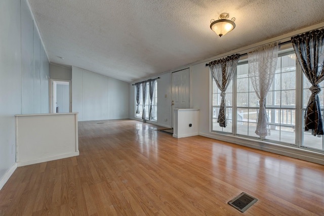 unfurnished living room featuring a textured ceiling, visible vents, vaulted ceiling, and wood finished floors