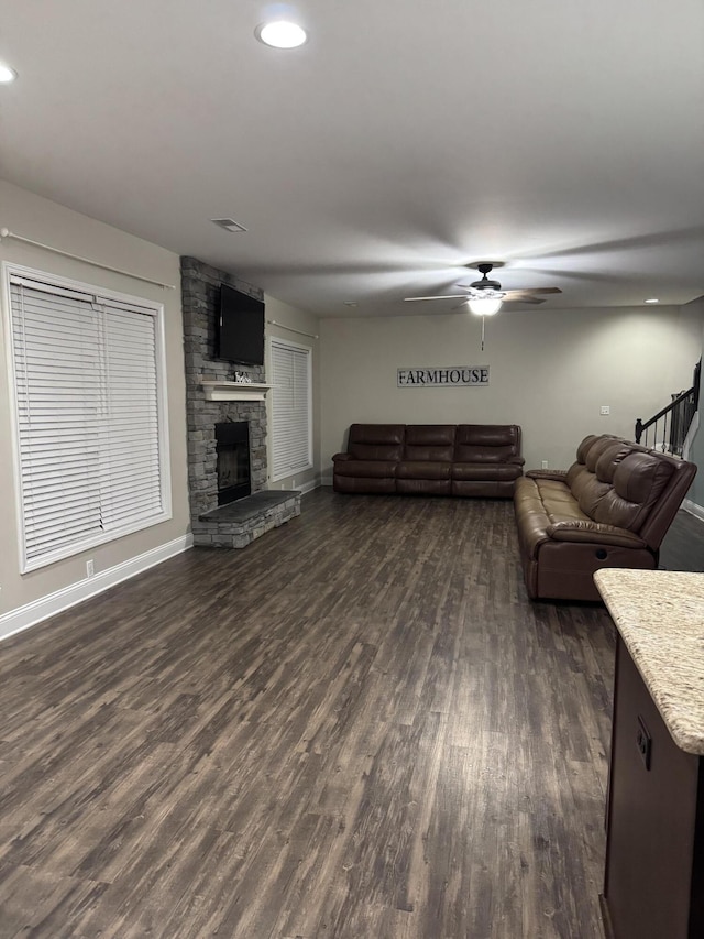 living room with dark wood-style floors, recessed lighting, ceiling fan, a stone fireplace, and stairs