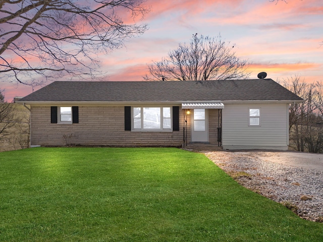 single story home with a shingled roof, a front lawn, and brick siding