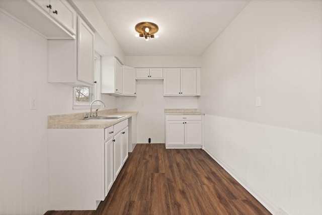 kitchen with dark wood-type flooring, light countertops, white cabinetry, and a sink