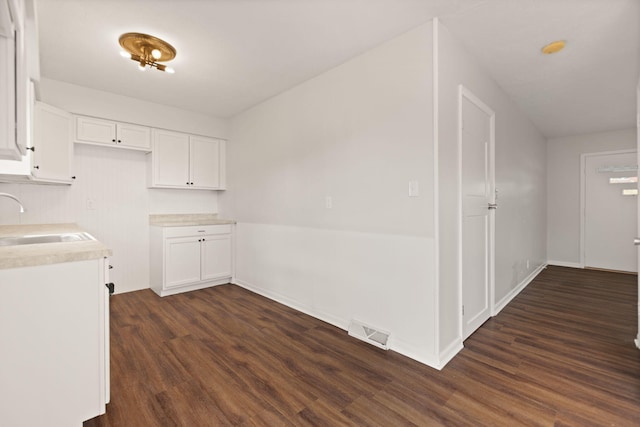 kitchen with dark wood-type flooring, white cabinets, visible vents, and a sink