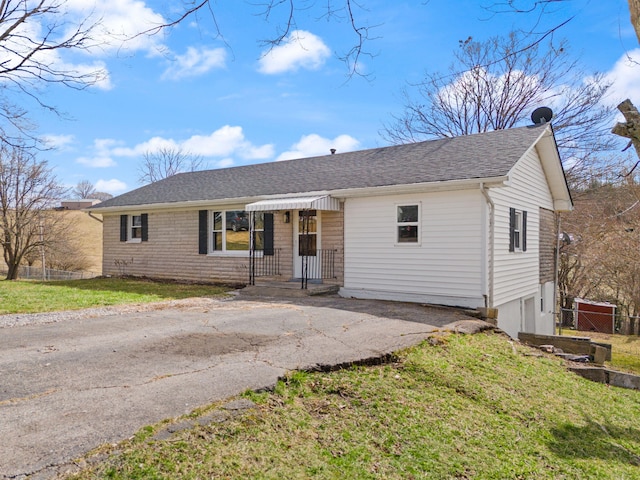 ranch-style house with driveway, a front lawn, roof with shingles, and fence