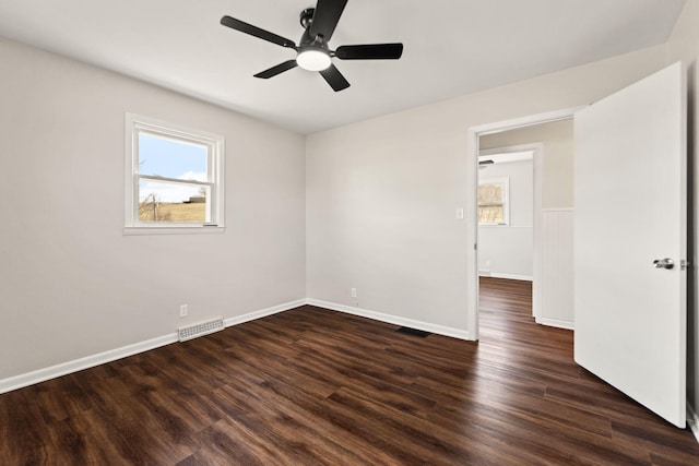 empty room with dark wood-style flooring, plenty of natural light, visible vents, and baseboards