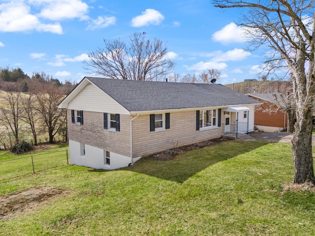 rear view of property featuring roof with shingles, brick siding, fence, and a lawn