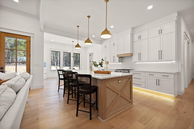 kitchen with light countertops, wall chimney range hood, light wood-type flooring, and backsplash