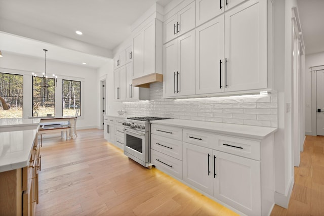 kitchen with recessed lighting, white cabinetry, light wood-style floors, high end stainless steel range oven, and backsplash