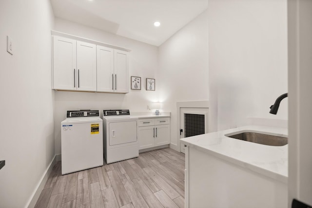 washroom featuring cabinet space, light wood finished floors, baseboards, washer and clothes dryer, and a sink