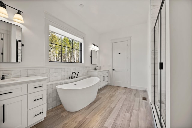 full bathroom with a sink, wood finished floors, two vanities, a soaking tub, and a shower stall