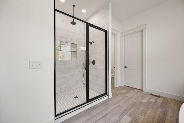 bathroom featuring a stall shower, baseboards, toilet, wood finished floors, and recessed lighting