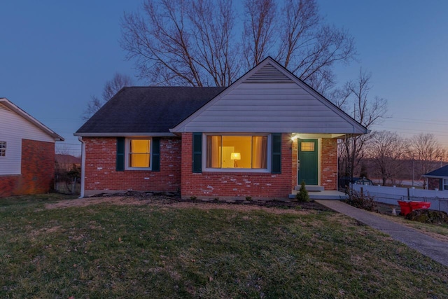 view of front of house featuring roof with shingles, fence, a lawn, and brick siding