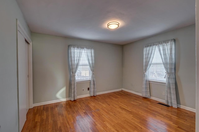 empty room featuring baseboards, visible vents, a wealth of natural light, and light wood-style floors