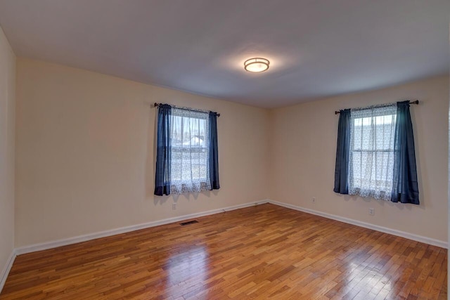 empty room featuring light wood-type flooring, visible vents, and baseboards