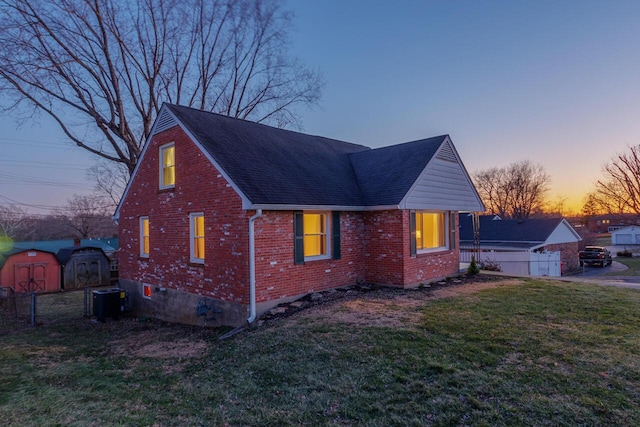 view of front of property featuring brick siding, a storage unit, a lawn, cooling unit, and an outdoor structure