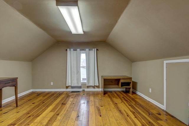 additional living space with hardwood / wood-style flooring, visible vents, baseboards, and vaulted ceiling