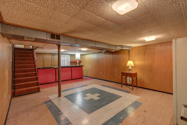 finished basement featuring wood finished floors, visible vents, wood walls, and stairs