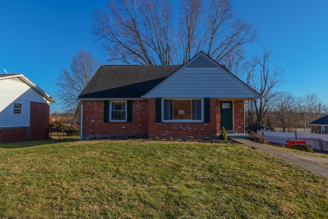 view of front facade with brick siding, roof with shingles, a front yard, and fence