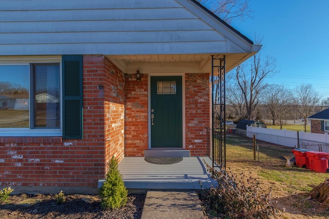 doorway to property featuring brick siding and fence