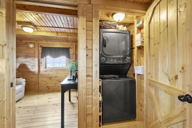 laundry room featuring laundry area, wooden ceiling, hardwood / wood-style floors, stacked washer / drying machine, and wood walls