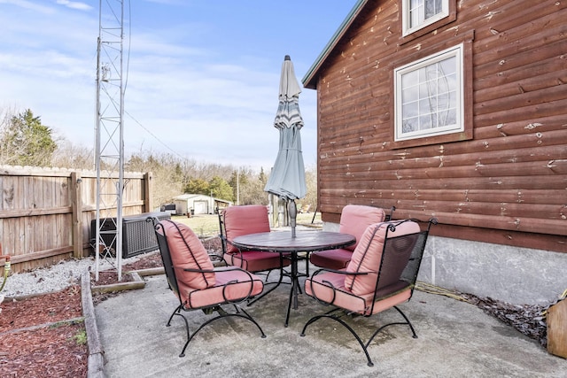 view of patio with an outbuilding, outdoor dining area, fence, and a storage unit