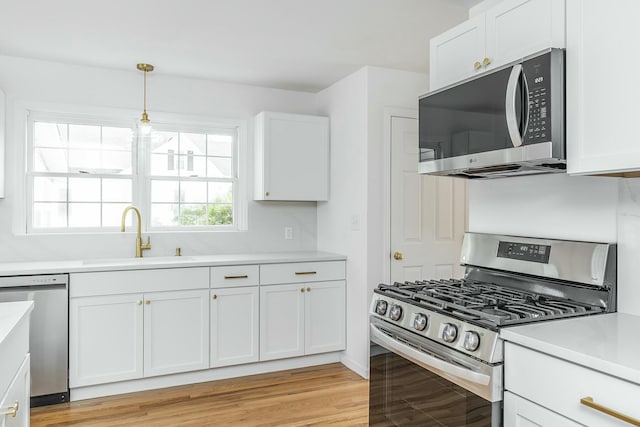 kitchen with stainless steel appliances, light countertops, light wood-style flooring, white cabinetry, and a sink