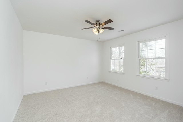 spare room with light colored carpet, visible vents, ceiling fan, and baseboards