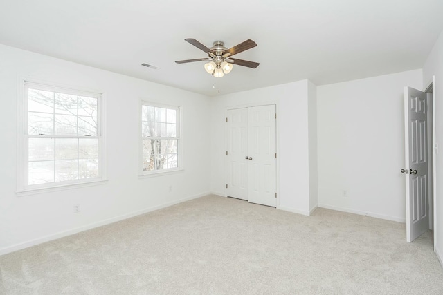 unfurnished bedroom with baseboards, visible vents, a ceiling fan, light colored carpet, and a closet