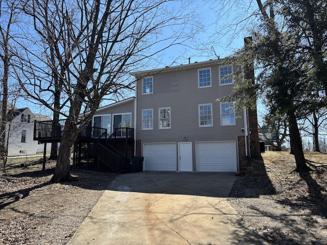 back of property featuring brick siding, a chimney, an attached garage, driveway, and stairs