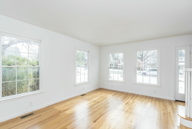 spare room with light wood finished floors, visible vents, and baseboards