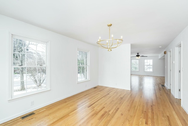 spare room featuring ceiling fan with notable chandelier, light wood-style flooring, visible vents, and baseboards