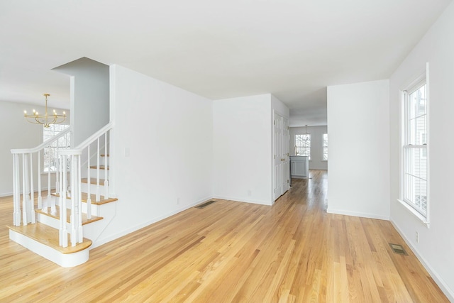 spare room with light wood-style floors, stairs, visible vents, and a notable chandelier