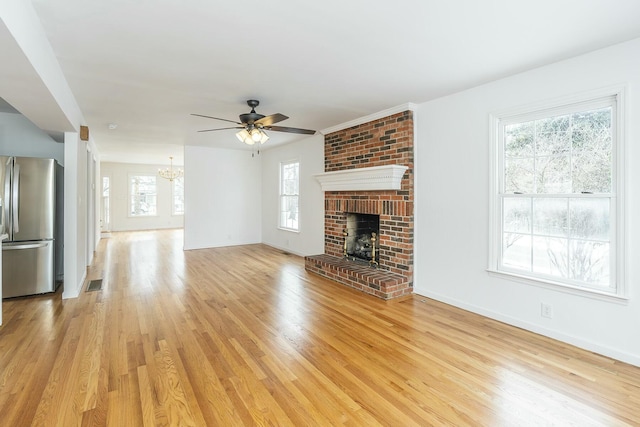 unfurnished living room with visible vents, light wood-style flooring, a brick fireplace, baseboards, and ceiling fan with notable chandelier