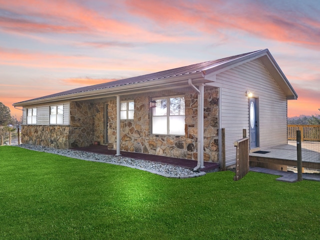 back of property featuring stone siding, metal roof, and a lawn