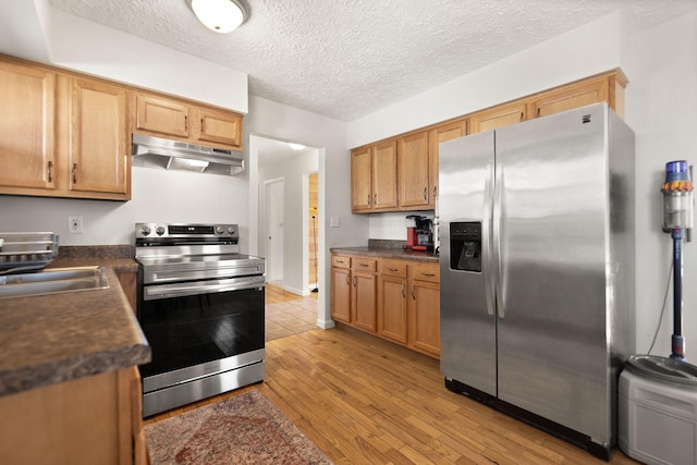 kitchen with dark countertops, light wood-style flooring, stainless steel appliances, a textured ceiling, and under cabinet range hood