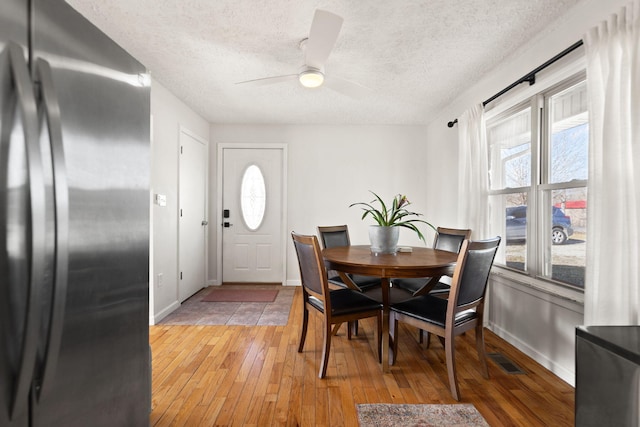 dining room with baseboards, visible vents, a textured ceiling, and light wood finished floors