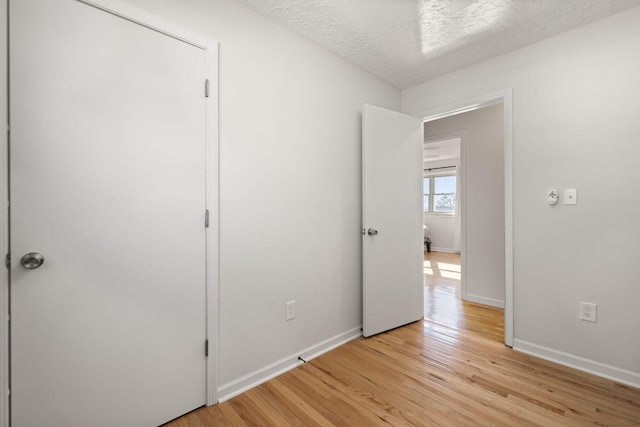 unfurnished bedroom featuring baseboards, a textured ceiling, and light wood finished floors