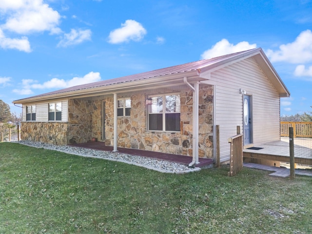 rear view of house featuring stone siding, a deck, metal roof, and a yard