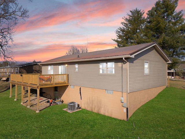 back of property at dusk with metal roof, a lawn, cooling unit, and a wooden deck