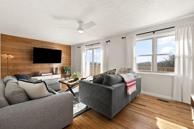 living area with visible vents, light wood-style flooring, an accent wall, wood walls, and a textured ceiling