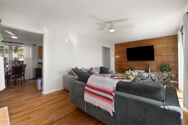 living room featuring light wood-style flooring, an accent wall, ceiling fan, wooden walls, and a textured ceiling