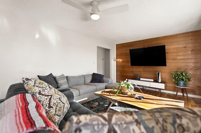 living area with a textured ceiling, ceiling fan, wooden walls, an accent wall, and wood finished floors