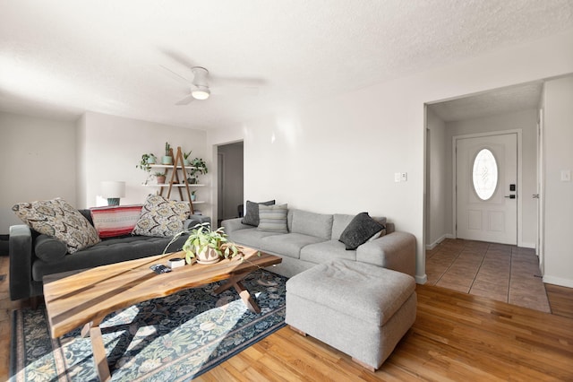 living area featuring a ceiling fan, a textured ceiling, baseboards, and wood finished floors