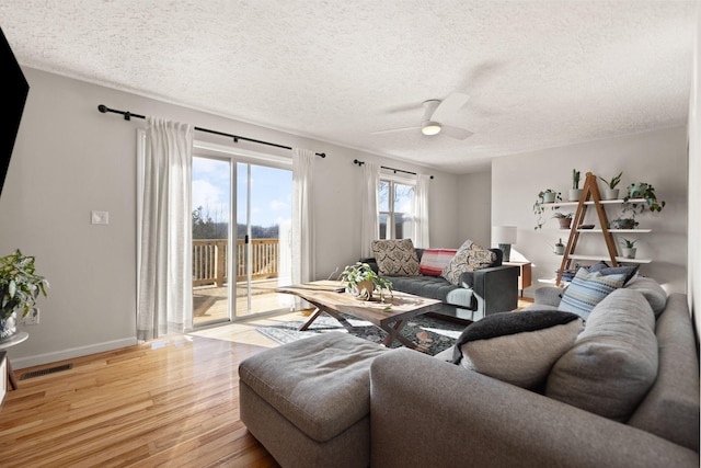 living area with light wood finished floors, visible vents, a ceiling fan, a textured ceiling, and baseboards