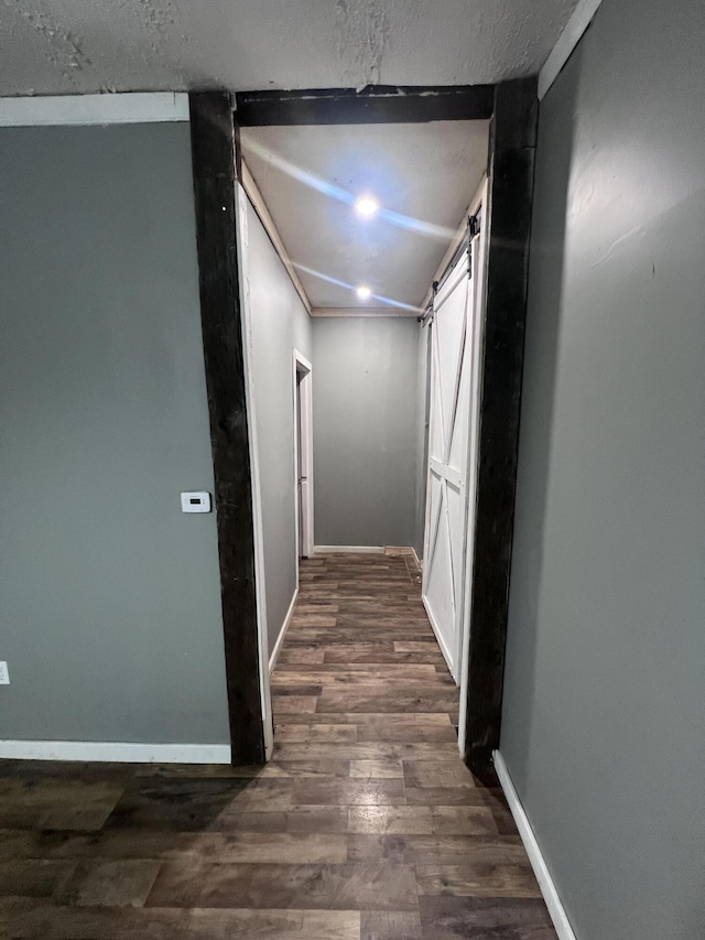 corridor with a barn door, wood finished floors, and baseboards