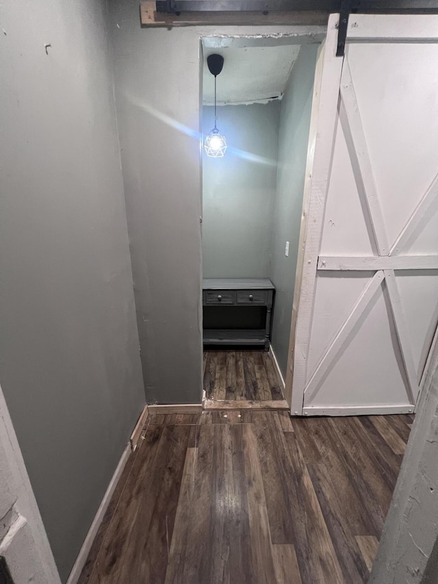 corridor featuring a barn door, wood finished floors, and baseboards