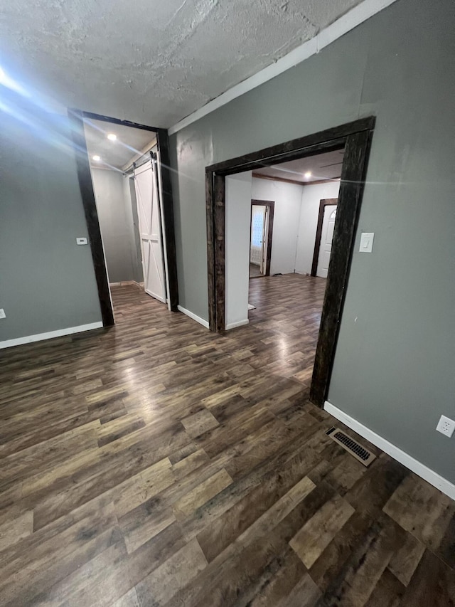 spare room with a textured ceiling, a barn door, wood finished floors, and visible vents