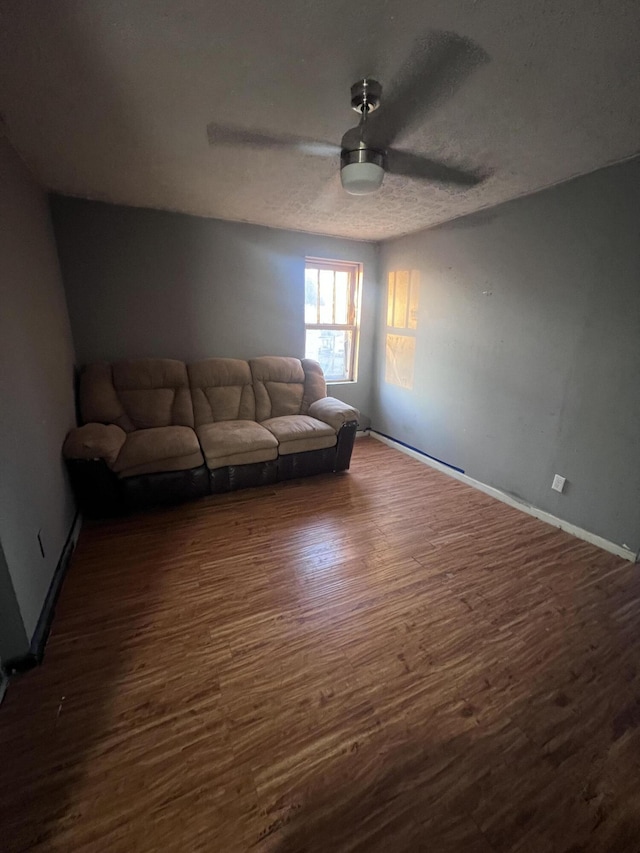 unfurnished living room featuring a ceiling fan, dark wood-style flooring, a textured ceiling, and baseboards