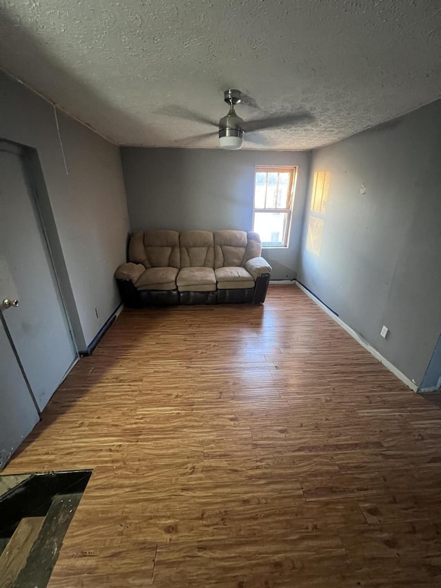 unfurnished living room with a textured ceiling, wood finished floors, a ceiling fan, and baseboards