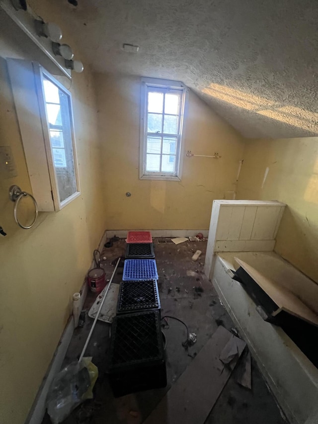 interior space with a bathing tub, vaulted ceiling, and a textured ceiling